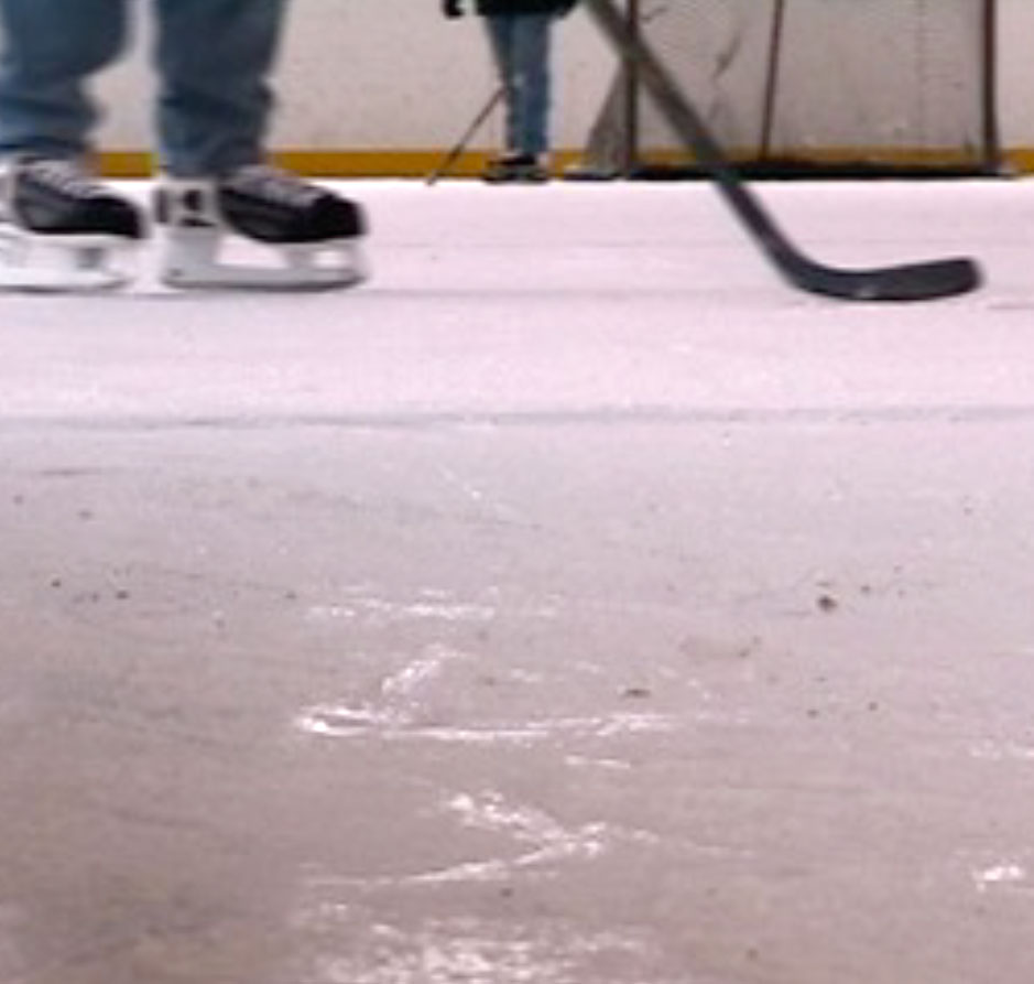 Low-angle view of ice rink with skates and a hockey stick on the ice, muted white and blue tones, active sporting mood.